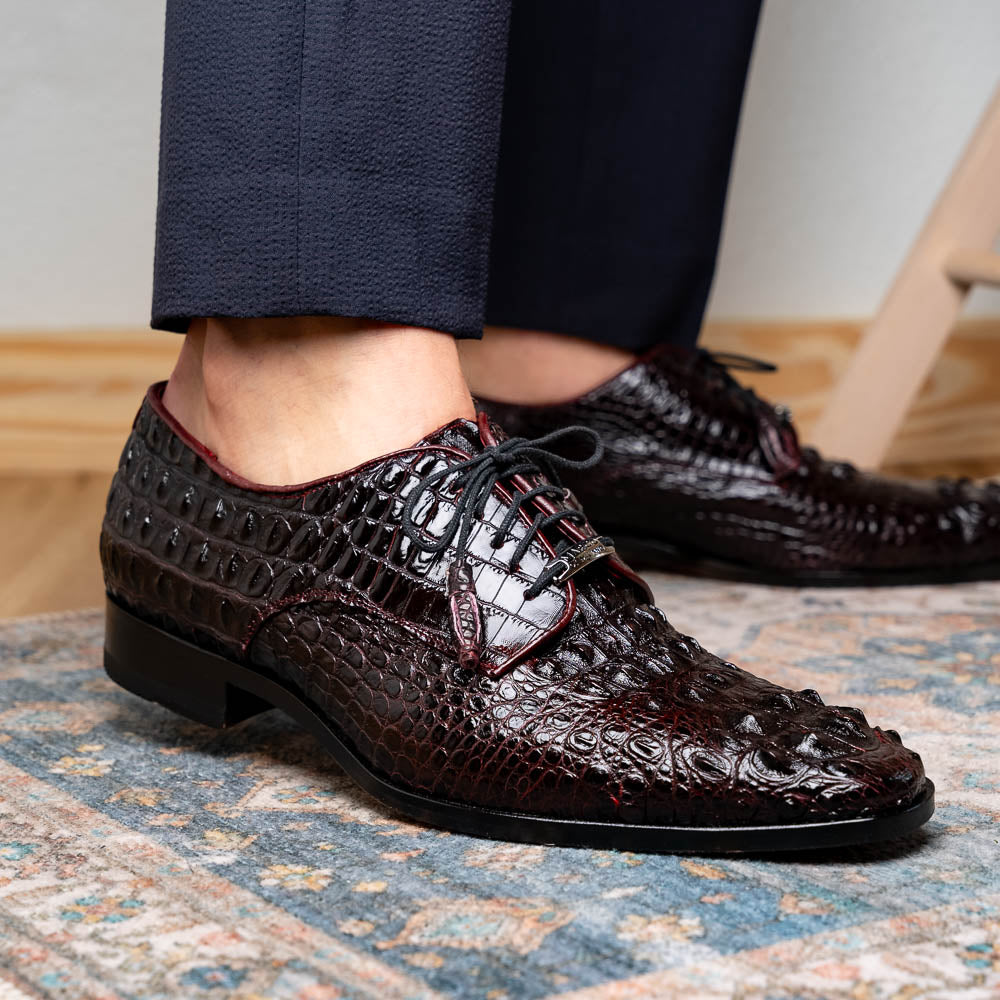 The Marco Di Milano Nilo Wine shoes are luxury dress footwear crafted from dark brown, textured Italian leather, featuring red interior lining and tan leather soles, with one shoe stylishly propped on the other.