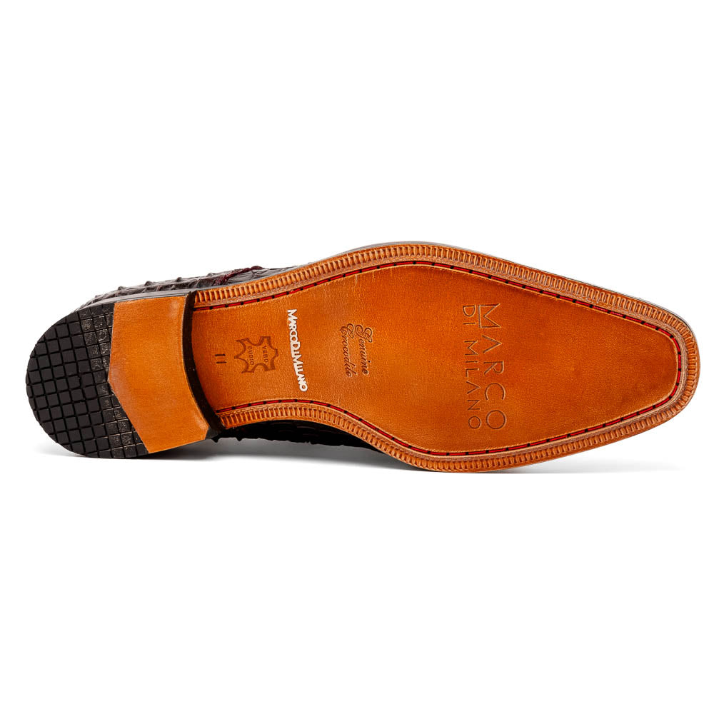 The Marco Di Milano Nilo Wine shoes are luxury dress footwear crafted from dark brown, textured Italian leather, featuring red interior lining and tan leather soles, with one shoe stylishly propped on the other.