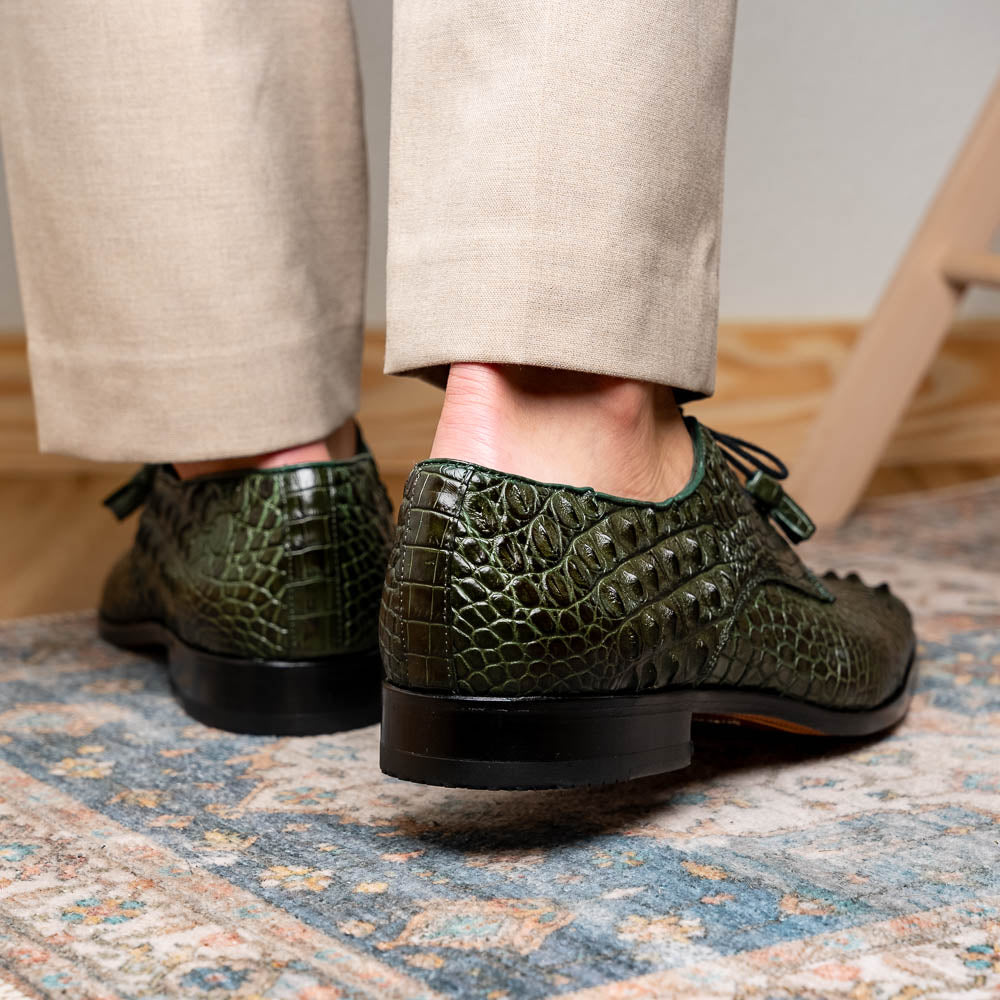The Nilo Forest Green by Marco Di Milano is a luxury pair crafted from premium Nile crocodile skin in green, with black laces—one shoe upright, the other showing a branded brown leather sole.