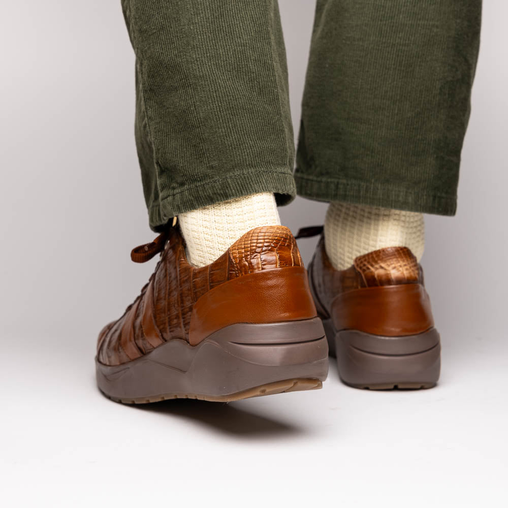 The Marco Di Milano Nino Bay Apache: luxurious brown genuine caiman crocodile sneakers, hand-painted with dark brown laces and grooved rubber soles—one stands upright while the other is shown lying on its side.