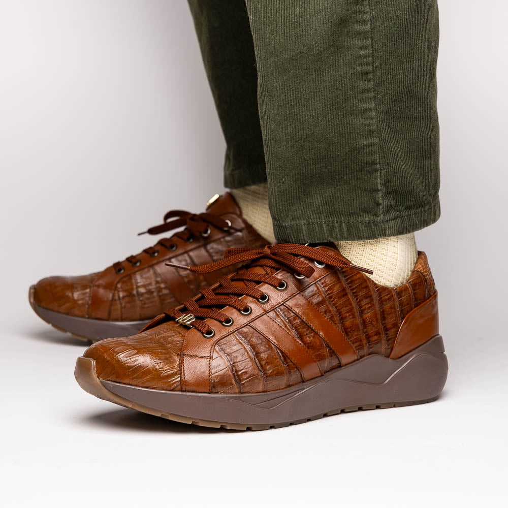 The Marco Di Milano Nino Bay Apache: luxurious brown genuine caiman crocodile sneakers, hand-painted with dark brown laces and grooved rubber soles—one stands upright while the other is shown lying on its side.