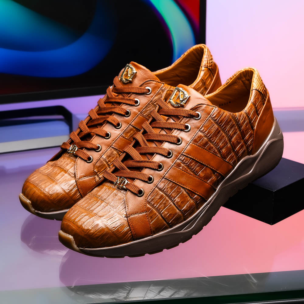 The Marco Di Milano Nino Bay Apache: luxurious brown genuine caiman crocodile sneakers, hand-painted with dark brown laces and grooved rubber soles—one stands upright while the other is shown lying on its side.