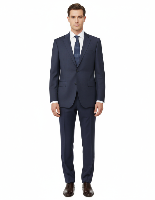 A man stands facing forward against a plain white background, wearing the Tiglio Luxe Novello Blue Birdseye Pure Wool Men’s Suit IDM7018/9, paired with a white shirt, blue tie, and brown dress shoes.