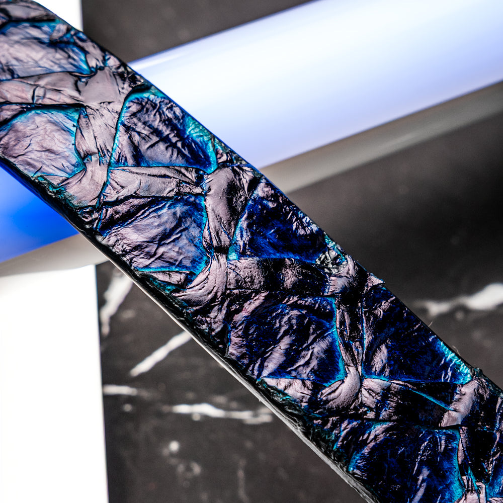 The Olivieri Belt Royal Blue by Marco Di Milano, featuring blue textured genuine pirarucu leather and a silver buckle, is coiled elegantly against a white background—an exquisite example of an exotic belt designed for the discerning gentleman.