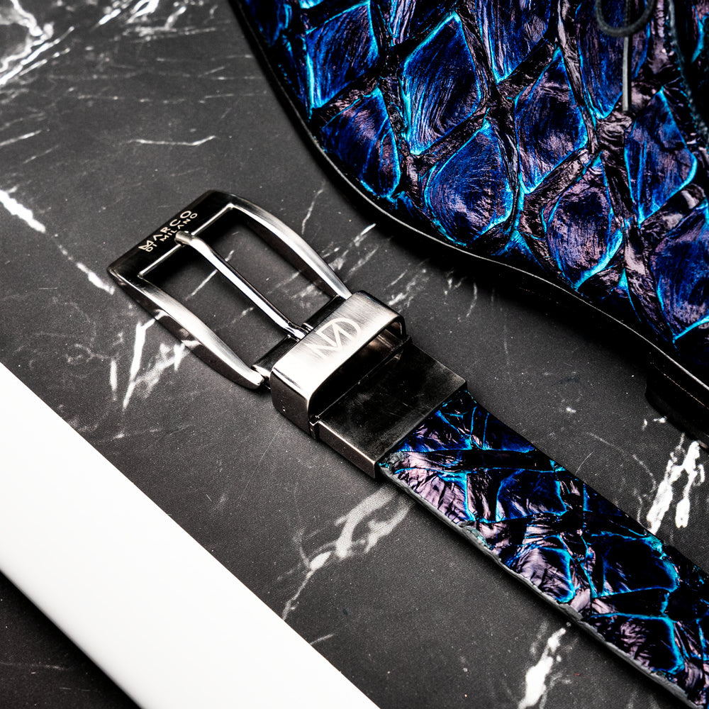 The Olivieri Belt Royal Blue by Marco Di Milano, featuring blue textured genuine pirarucu leather and a silver buckle, is coiled elegantly against a white background—an exquisite example of an exotic belt designed for the discerning gentleman.