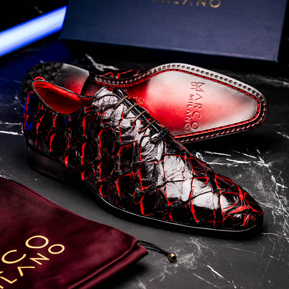 A pair of Marco Di Milano Olivieri Blackcherry oxfords—one upright, one on its side—displays the brand name on the sole, offering luxury men’s footwear with a strikingly exotic black and red pirarucu finish.