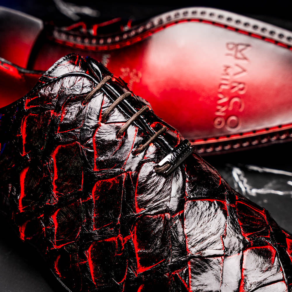 A pair of Marco Di Milano Olivieri Blackcherry oxfords—one upright, one on its side—displays the brand name on the sole, offering luxury men’s footwear with a strikingly exotic black and red pirarucu finish.