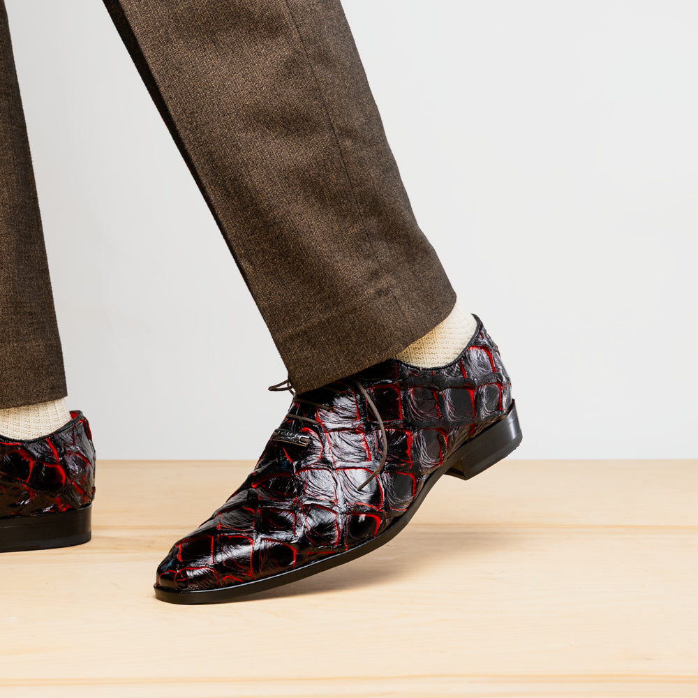 A pair of Marco Di Milano Olivieri Blackcherry oxfords—one upright, one on its side—displays the brand name on the sole, offering luxury men’s footwear with a strikingly exotic black and red pirarucu finish.