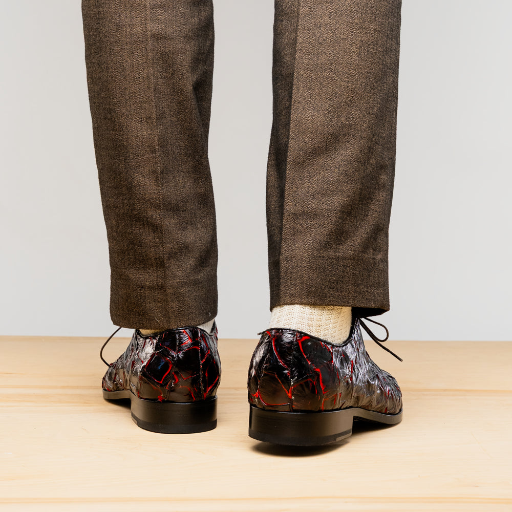 A pair of Marco Di Milano Olivieri Blackcherry oxfords—one upright, one on its side—displays the brand name on the sole, offering luxury men’s footwear with a strikingly exotic black and red pirarucu finish.
