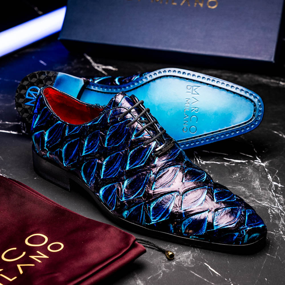 The Olivieri Royal Blue by Marco Di Milano is a pair of men's dress shoes featuring a blue and black textured design. One shoe stands upright, the other displays a bright blue sole with "Marco Di Milano" branding—true luxury.