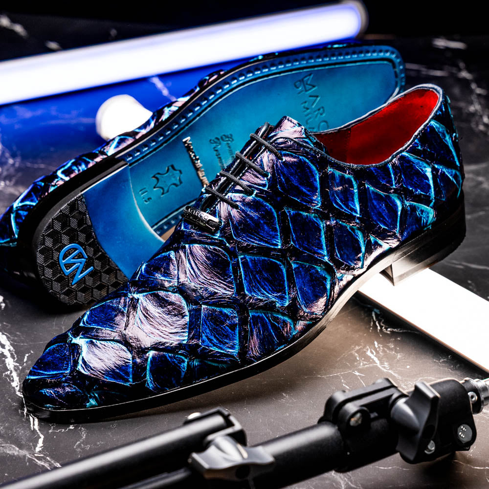 The Olivieri Royal Blue by Marco Di Milano is a pair of men's dress shoes featuring a blue and black textured design. One shoe stands upright, the other displays a bright blue sole with "Marco Di Milano" branding—true luxury.