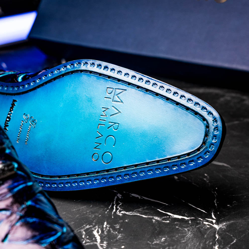 The Olivieri Royal Blue by Marco Di Milano is a pair of men's dress shoes featuring a blue and black textured design. One shoe stands upright, the other displays a bright blue sole with "Marco Di Milano" branding—true luxury.