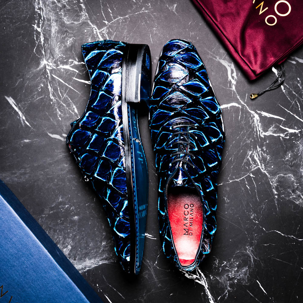 The Olivieri Royal Blue by Marco Di Milano is a pair of men's dress shoes featuring a blue and black textured design. One shoe stands upright, the other displays a bright blue sole with "Marco Di Milano" branding—true luxury.