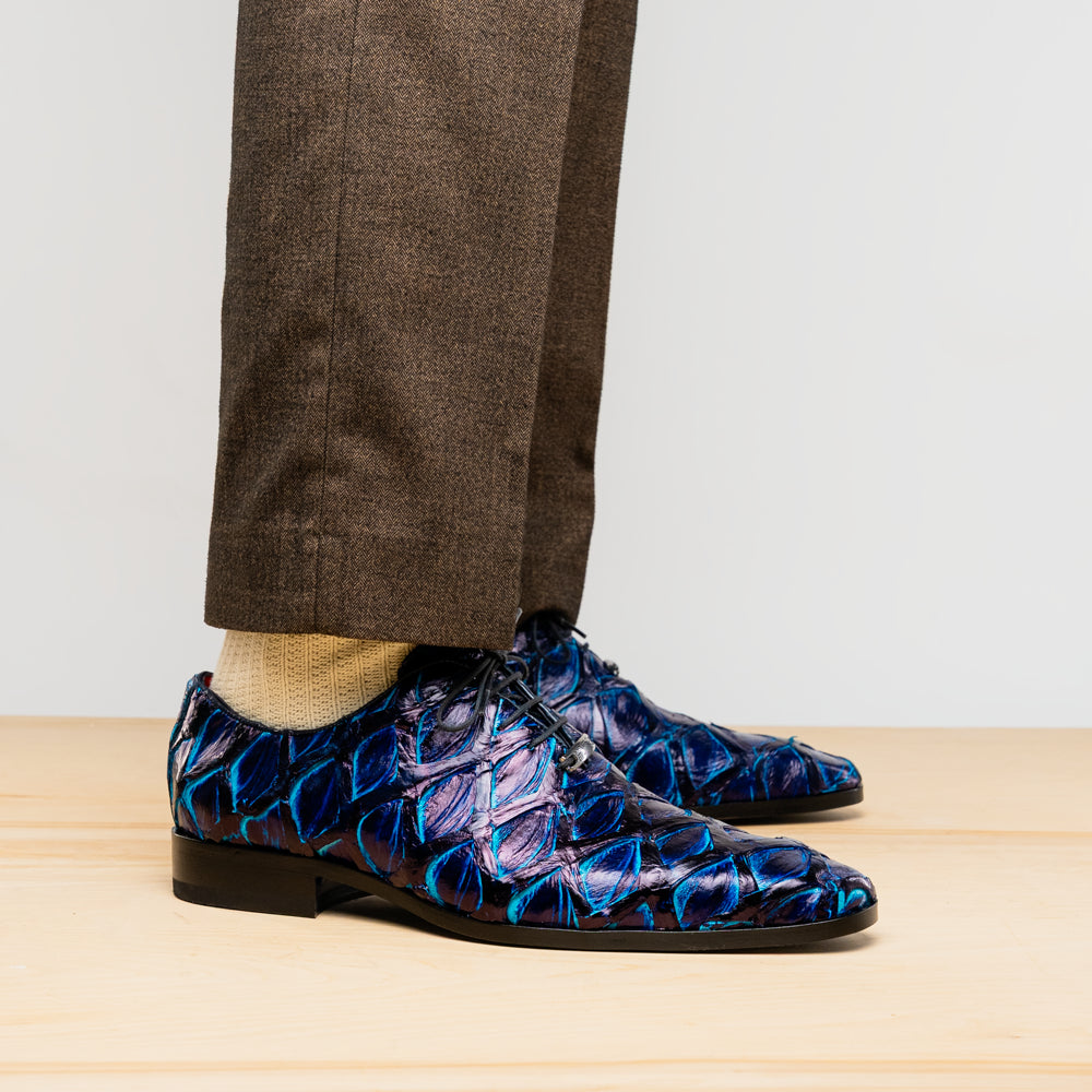 The Olivieri Royal Blue by Marco Di Milano is a pair of men's dress shoes featuring a blue and black textured design. One shoe stands upright, the other displays a bright blue sole with "Marco Di Milano" branding—true luxury.