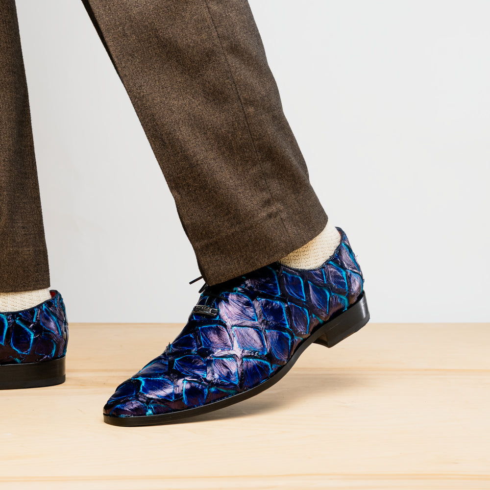The Olivieri Royal Blue by Marco Di Milano is a pair of men's dress shoes featuring a blue and black textured design. One shoe stands upright, the other displays a bright blue sole with "Marco Di Milano" branding—true luxury.