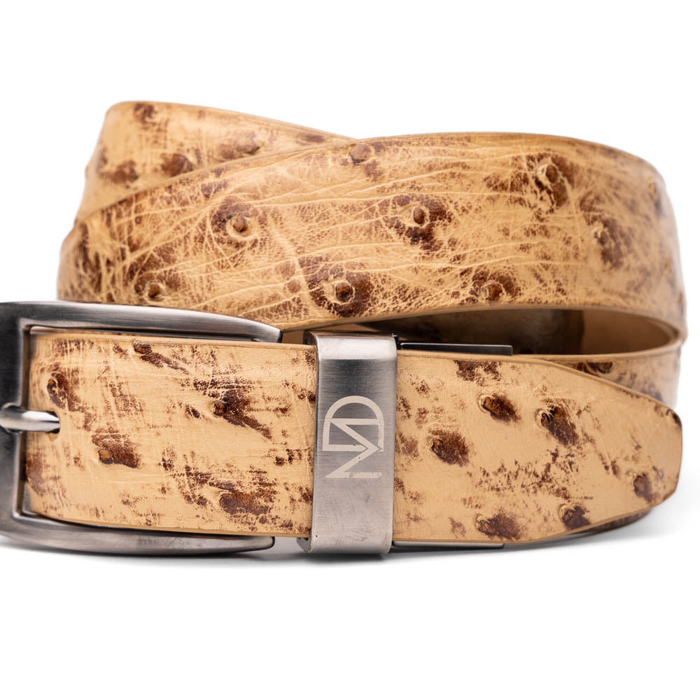 The Domenico Belt Antique Orix by Marco Di Milano—a light brown genuine ostrich belt with a silver engraved buckle, coiled on a white background—offers refined style to complement luxury footwear.