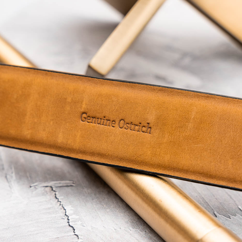 The Domenico Belt Brandy by Marco Di Milano, featuring rich brown ostrich leather and a silver branded buckle, is coiled on a white background—an elegant accessory to complement luxury footwear.