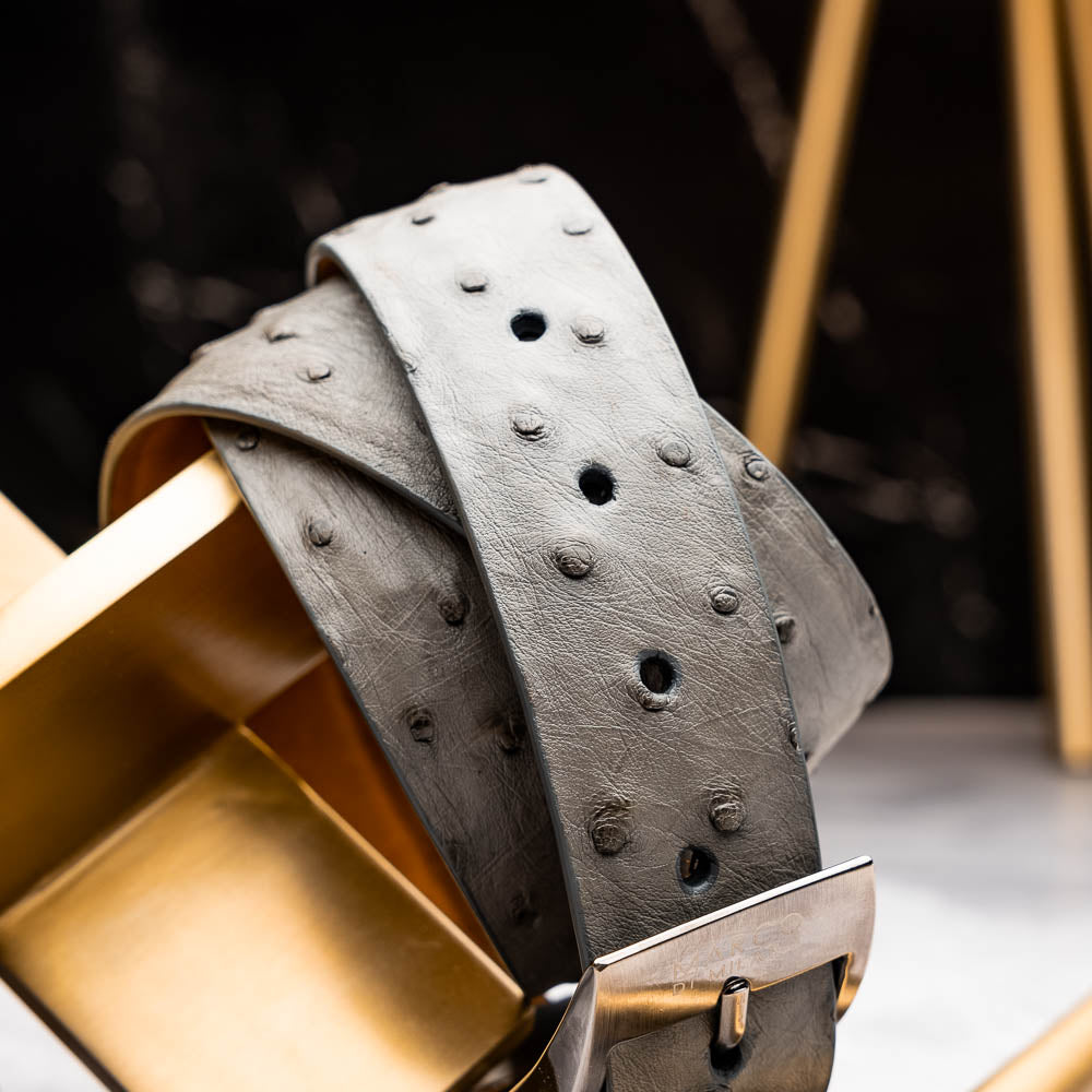 The Domenico Belt Gray by Marco Di Milano is crafted from grey ostrich leather and features a silver buckle engraved with "Marco Di Milano" and the "MD" logo, reflecting the brand's luxurious craftsmanship. Shown coiled on a white background.