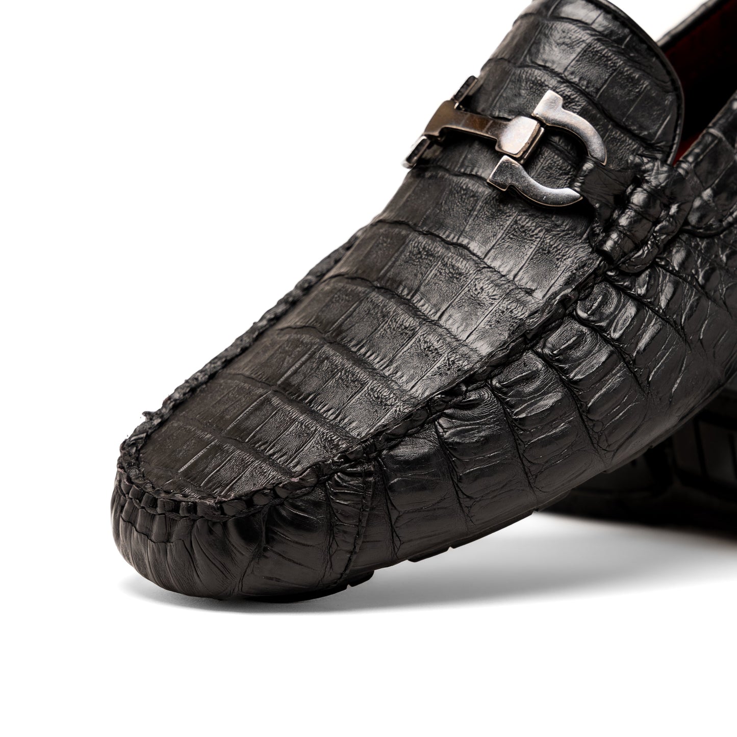 The Marco Di Milano Parma Black is a luxury caiman belly loafer featuring black crocodile-textured leather, metal buckle accents, and rubber soles, with one men’s driving shoe upright and the other leaning against it.