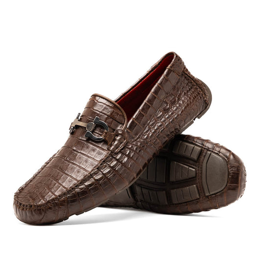 The Marco Di Milano Parma Brown features a pair of brown caiman belly loafers with black metal buckles—one upright, the other on its side showing the sole—a luxurious footwear choice.