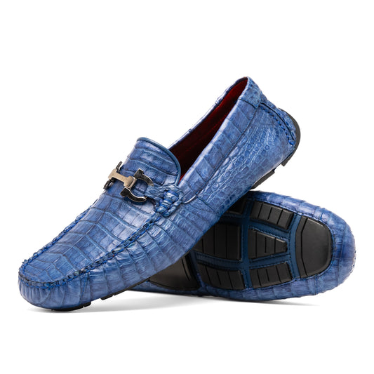 The Marco Di Milano Parma Blue Jeans loafers feature genuine blue caiman leather with a crocodile pattern, metal hardware accents, and rubber soles—ideal luxury footwear, displayed with one shoe upright and the other on its side.