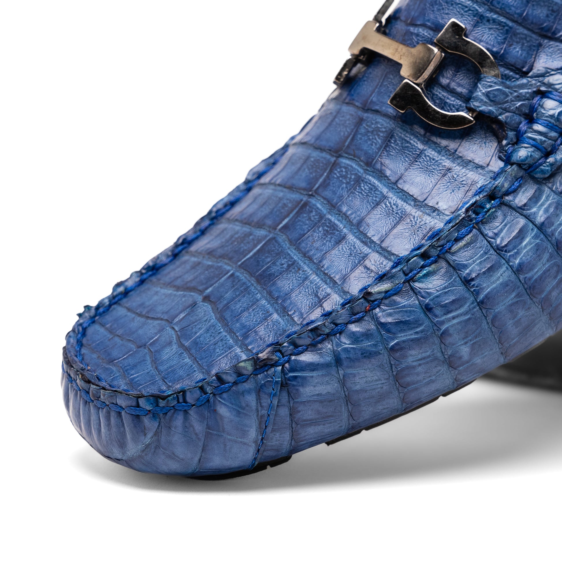 The Marco Di Milano Parma Blue Jeans loafers feature genuine blue caiman leather with a crocodile pattern, metal hardware accents, and rubber soles—ideal luxury footwear, displayed with one shoe upright and the other on its side.