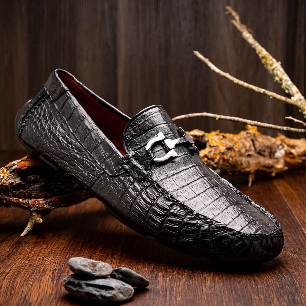 The Marco Di Milano Parma Black is a luxury caiman belly loafer featuring black crocodile-textured leather, metal buckle accents, and rubber soles, with one men’s driving shoe upright and the other leaning against it.