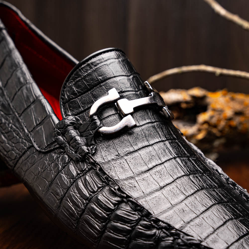 The Marco Di Milano Parma Black is a luxury caiman belly loafer featuring black crocodile-textured leather, metal buckle accents, and rubber soles, with one men’s driving shoe upright and the other leaning against it.