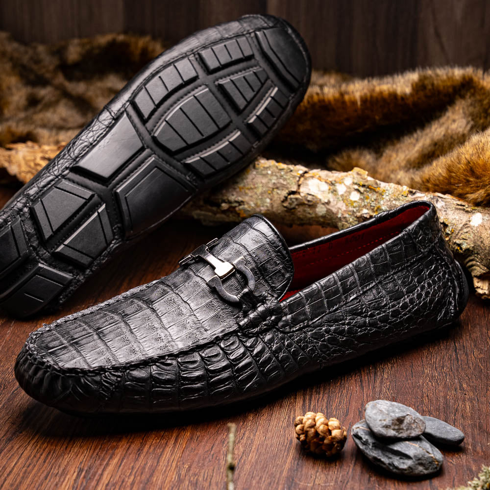 The Marco Di Milano Parma Black is a luxury caiman belly loafer featuring black crocodile-textured leather, metal buckle accents, and rubber soles, with one men’s driving shoe upright and the other leaning against it.