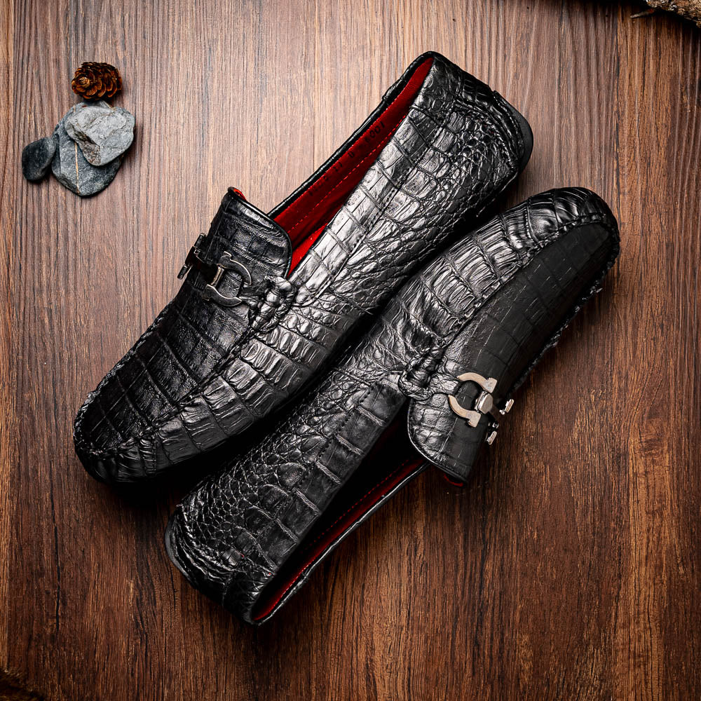 The Marco Di Milano Parma Black is a luxury caiman belly loafer featuring black crocodile-textured leather, metal buckle accents, and rubber soles, with one men’s driving shoe upright and the other leaning against it.
