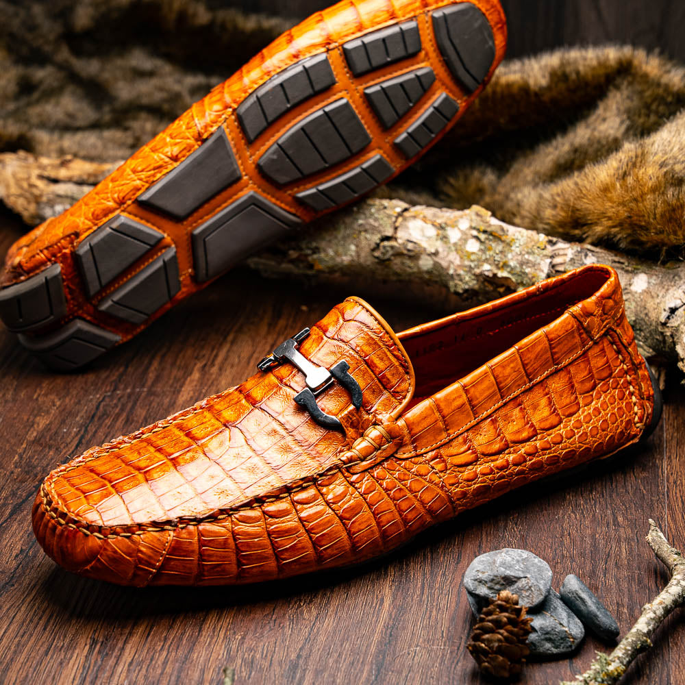 Marco Di Milano’s Parma Brandy loafers feature an orange crocodile pattern, black metal buckles, and hand-painted finishes—one shoe stands upright while the other lies on its side to reveal the detailed sole.