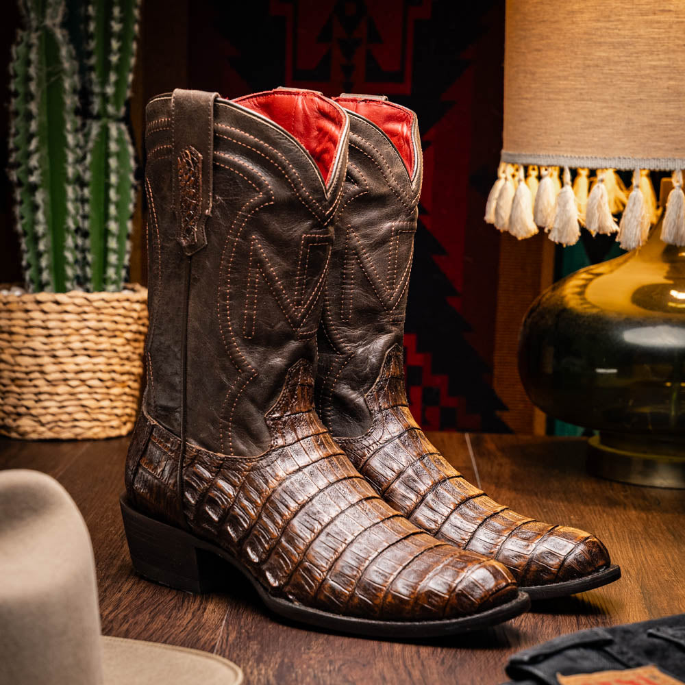 A pair of Marco Di Milano Phoenix Aged Brown men's boots, one upright and one showing the sole, crafted from genuine caiman belly skin with a crocodile texture and detailed stitching—ideal for any Western collection.