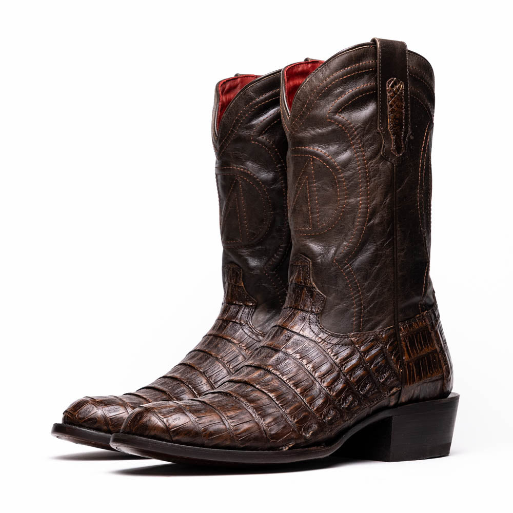A pair of Marco Di Milano Phoenix Aged Brown men's boots, one upright and one showing the sole, crafted from genuine caiman belly skin with a crocodile texture and detailed stitching—ideal for any Western collection.