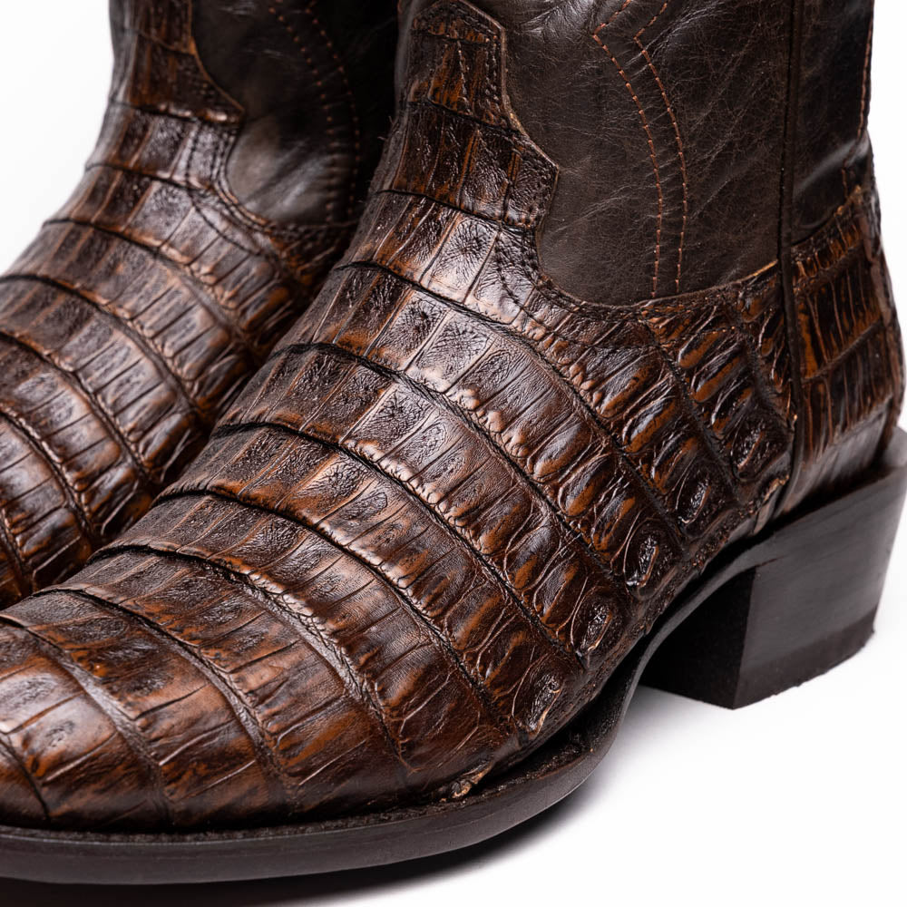 A pair of Marco Di Milano Phoenix Aged Brown men's boots, one upright and one showing the sole, crafted from genuine caiman belly skin with a crocodile texture and detailed stitching—ideal for any Western collection.