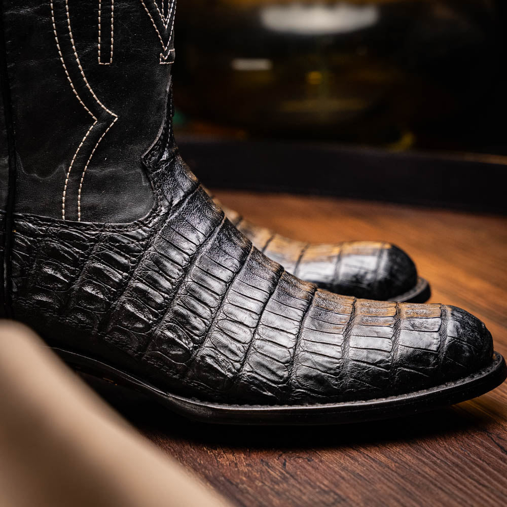 A pair of Phoenix Black Western cowboy boots by Marco Di Milano, one upright and one showing the sole, featuring a textured pattern and the brand name on the sole.