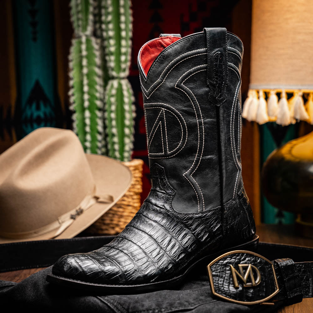 A pair of Phoenix Black Western cowboy boots by Marco Di Milano, one upright and one showing the sole, featuring a textured pattern and the brand name on the sole.
