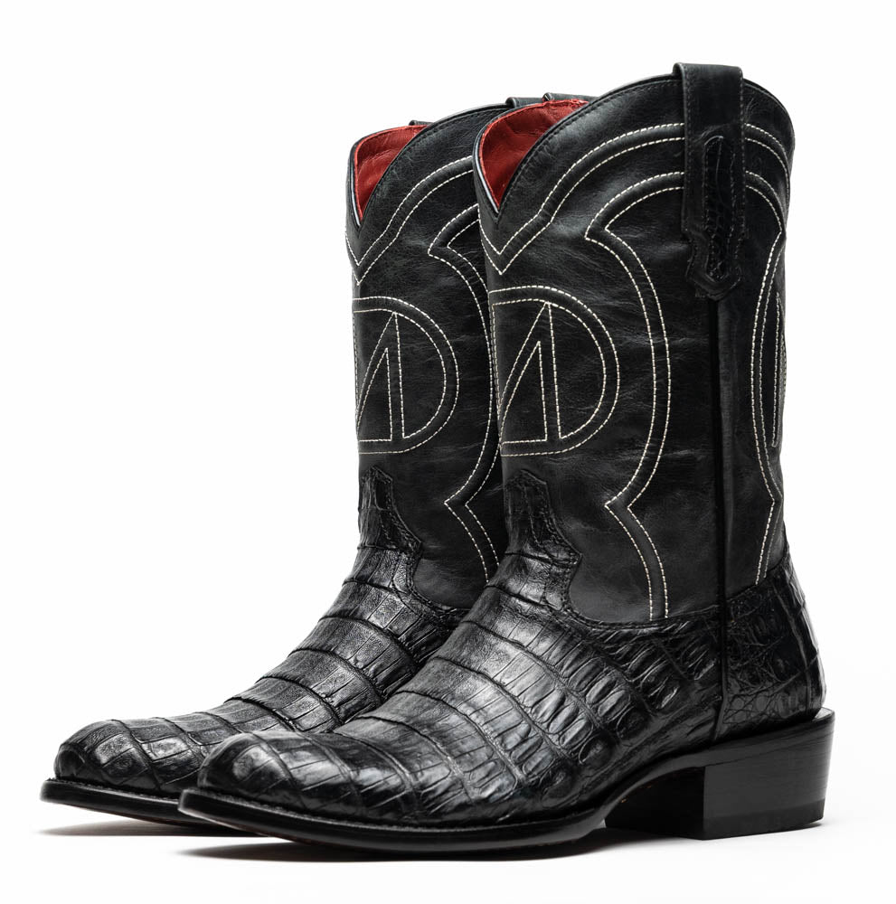 A pair of Phoenix Black Western cowboy boots by Marco Di Milano, one upright and one showing the sole, featuring a textured pattern and the brand name on the sole.
