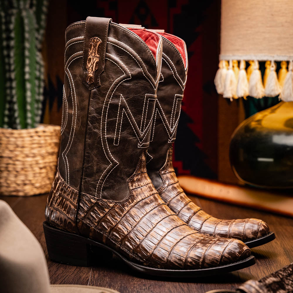 The Phoenix Stone Brown by Marco Di Milano are brown Western cowboy boots featuring crocodile-patterned textured leather, decorative stitching, and branded soles.