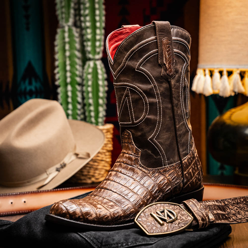 The Phoenix Stone Brown by Marco Di Milano are brown Western cowboy boots featuring crocodile-patterned textured leather, decorative stitching, and branded soles.