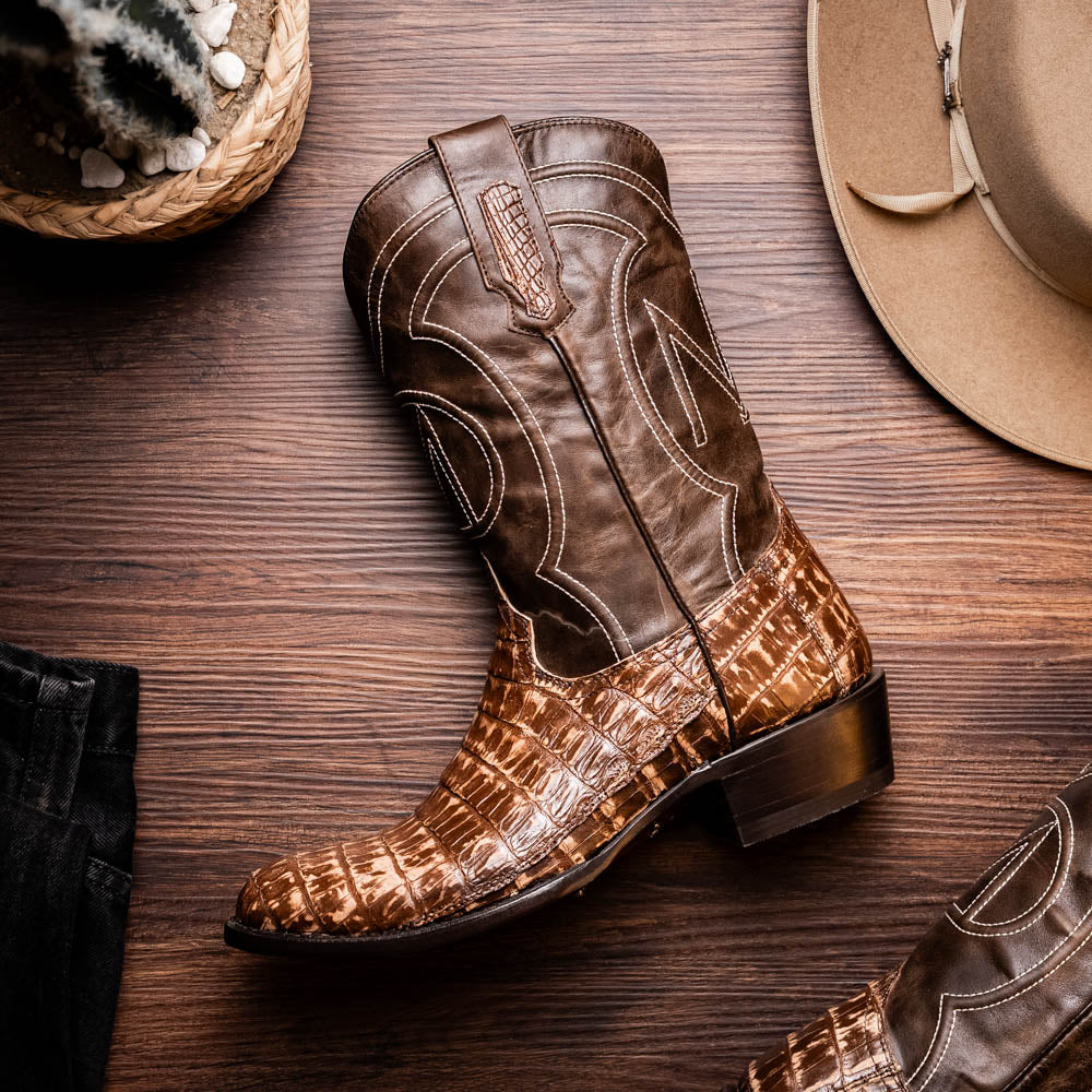 The Phoenix Stone Brown by Marco Di Milano are brown Western cowboy boots featuring crocodile-patterned textured leather, decorative stitching, and branded soles.