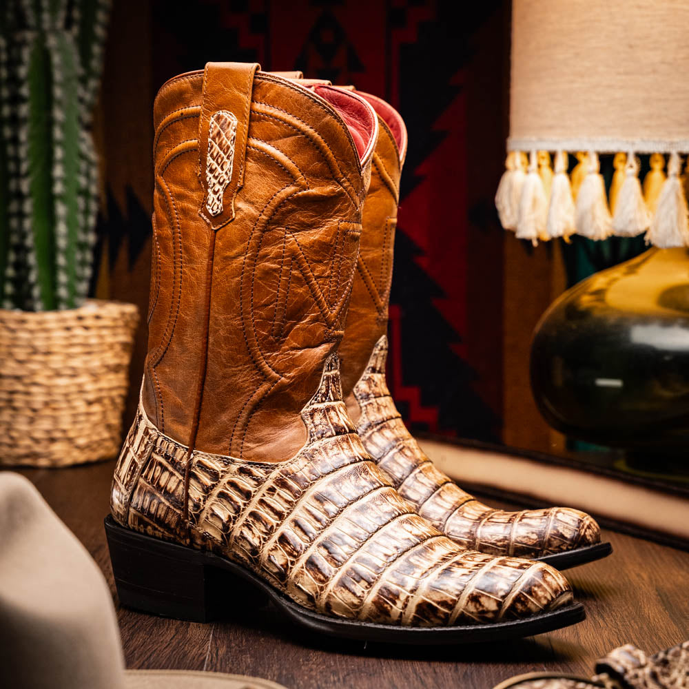 A pair of Phoenix Stone Orix brown Western cowboy boots by Marco Di Milano, featuring an alligator texture—one boot upright, the other displaying the sole with the brand logo.