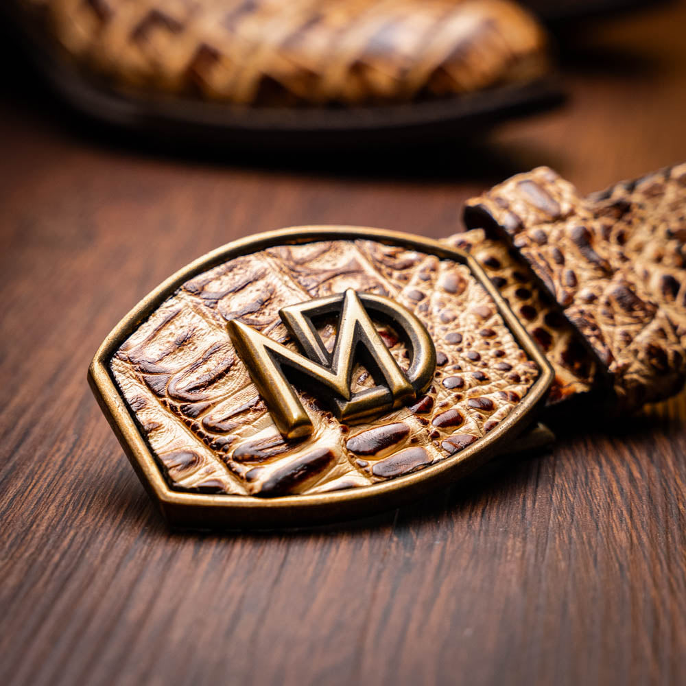 A pair of Phoenix Stone Orix brown Western cowboy boots by Marco Di Milano, featuring an alligator texture—one boot upright, the other displaying the sole with the brand logo.
