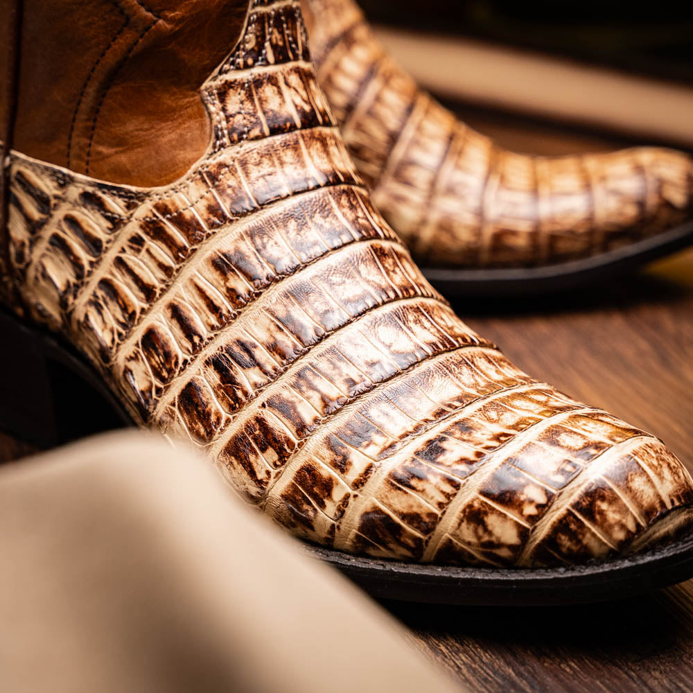 A pair of Phoenix Stone Orix brown Western cowboy boots by Marco Di Milano, featuring an alligator texture—one boot upright, the other displaying the sole with the brand logo.