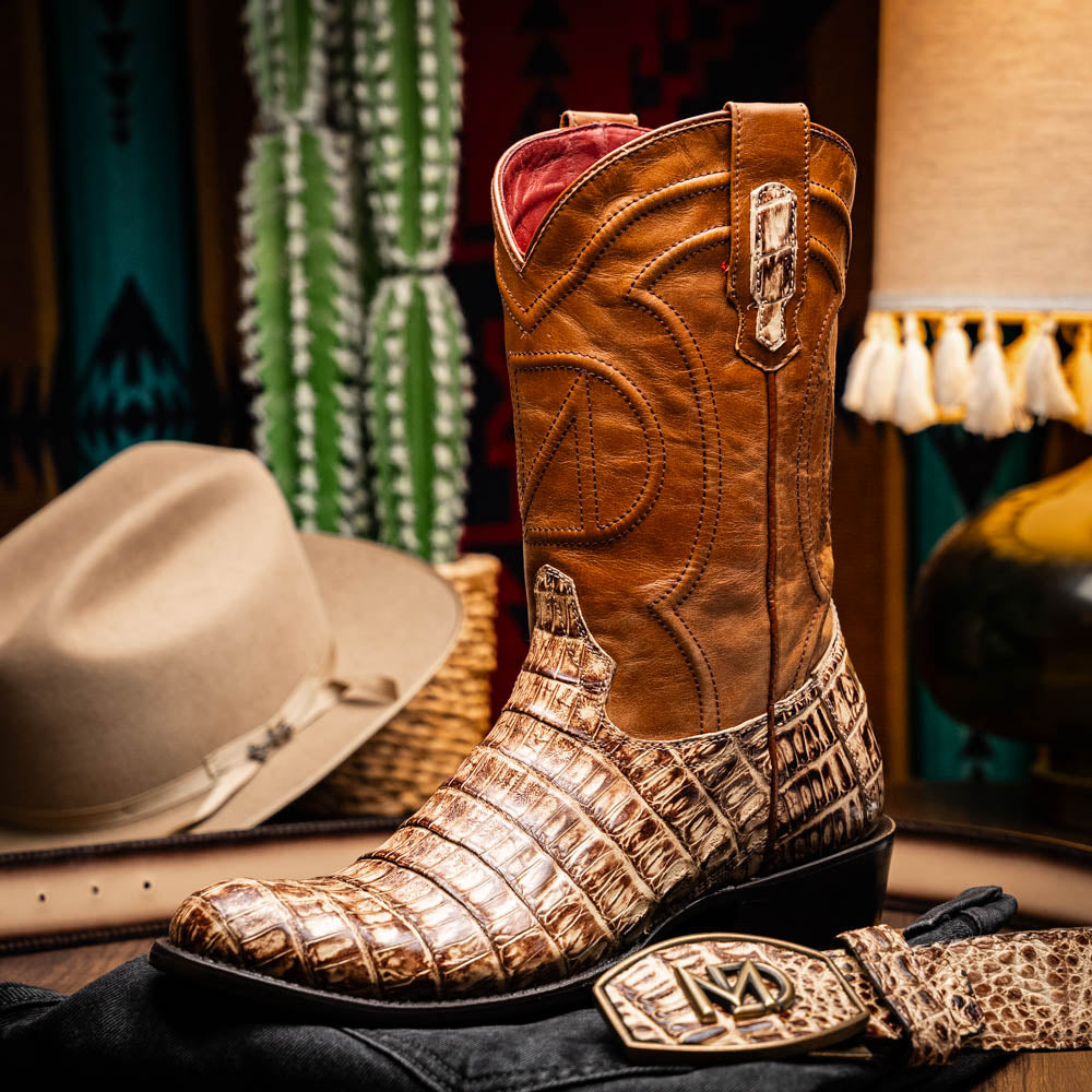 A pair of Phoenix Stone Orix brown Western cowboy boots by Marco Di Milano, featuring an alligator texture—one boot upright, the other displaying the sole with the brand logo.