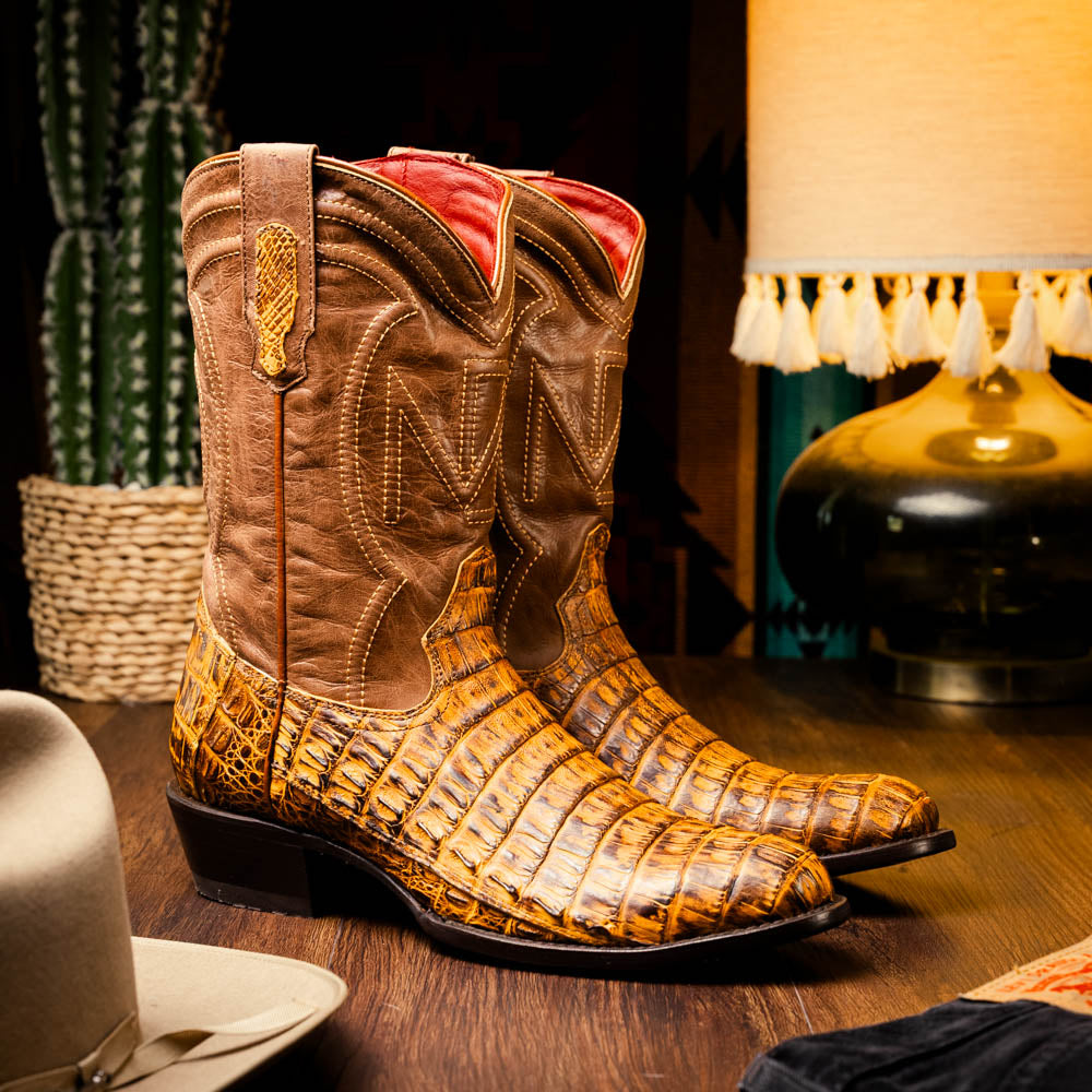 The Phoenix Mustard Brown by Marco Di Milano is a pair of Western boots in genuine caiman belly leather with a textured exotic finish and branded sole, shown against a white background.