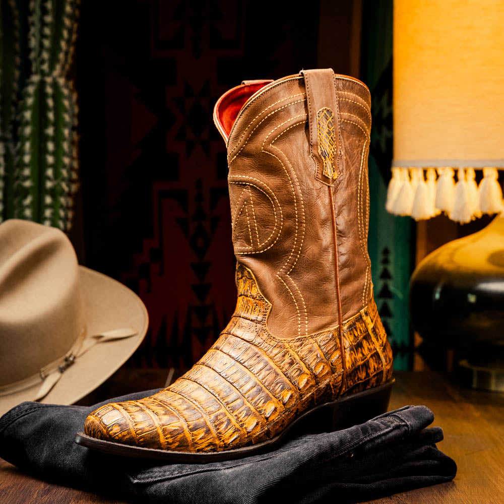The Phoenix Mustard Brown by Marco Di Milano is a pair of Western boots in genuine caiman belly leather with a textured exotic finish and branded sole, shown against a white background.