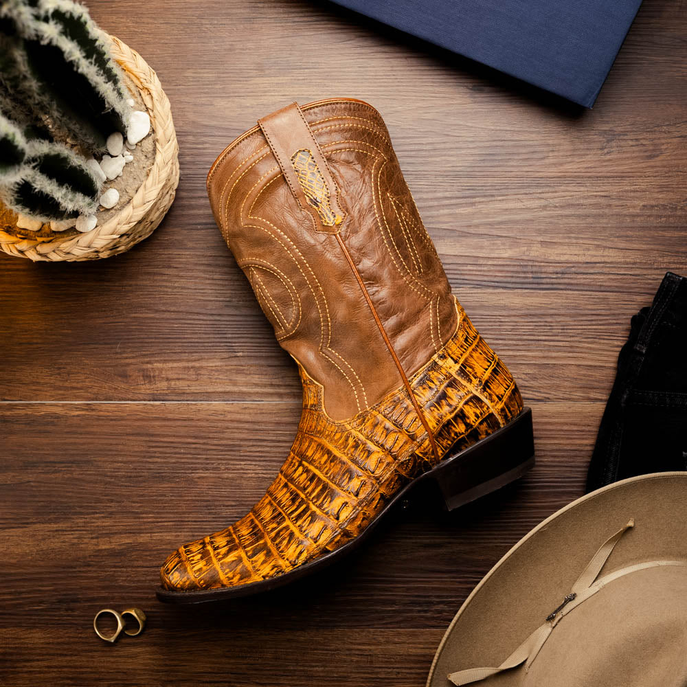The Phoenix Mustard Brown by Marco Di Milano is a pair of Western boots in genuine caiman belly leather with a textured exotic finish and branded sole, shown against a white background.
