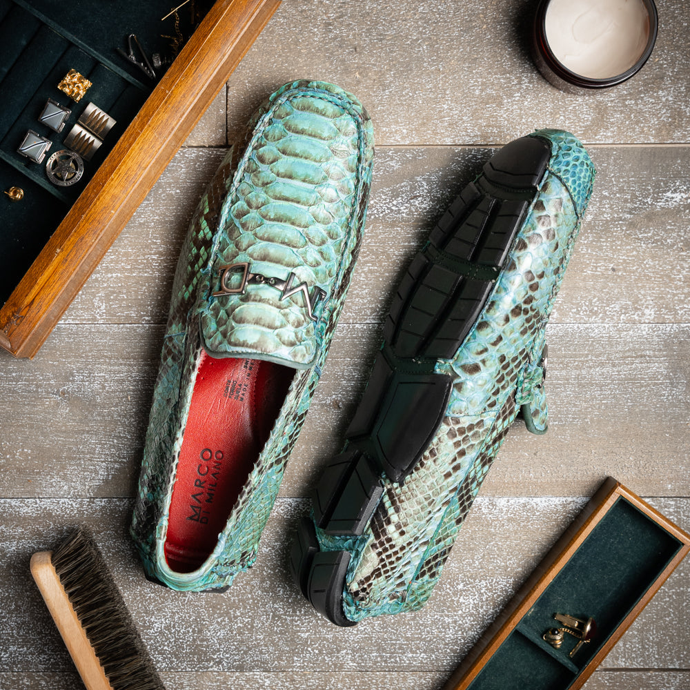 Introducing the Pia Aqua by Marco Di Milano—a pair of luxury men’s loafers handcrafted from striking green python skin. Featuring black rubber soles and silver buckle accents, one shoe is elegantly displayed on its side to highlight the distinctive design of this opulent driver shoe.