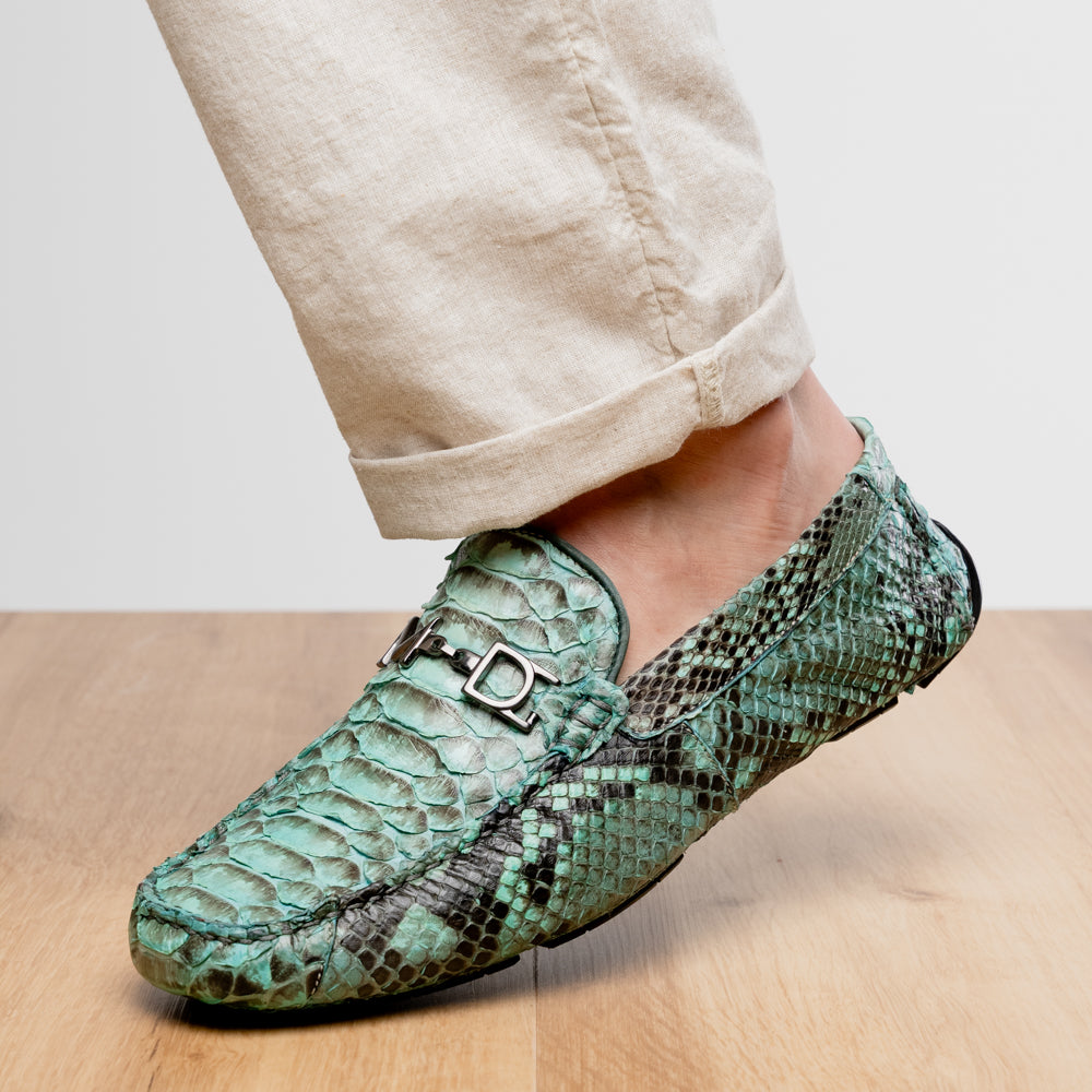 Introducing the Pia Aqua by Marco Di Milano—a pair of luxury men’s loafers handcrafted from striking green python skin. Featuring black rubber soles and silver buckle accents, one shoe is elegantly displayed on its side to highlight the distinctive design of this opulent driver shoe.