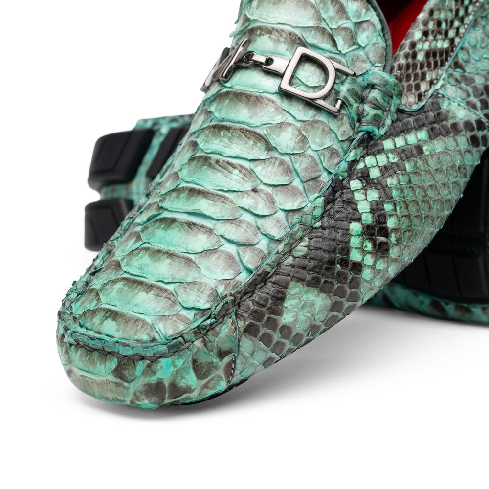 Introducing the Pia Aqua by Marco Di Milano—a pair of luxury men’s loafers handcrafted from striking green python skin. Featuring black rubber soles and silver buckle accents, one shoe is elegantly displayed on its side to highlight the distinctive design of this opulent driver shoe.